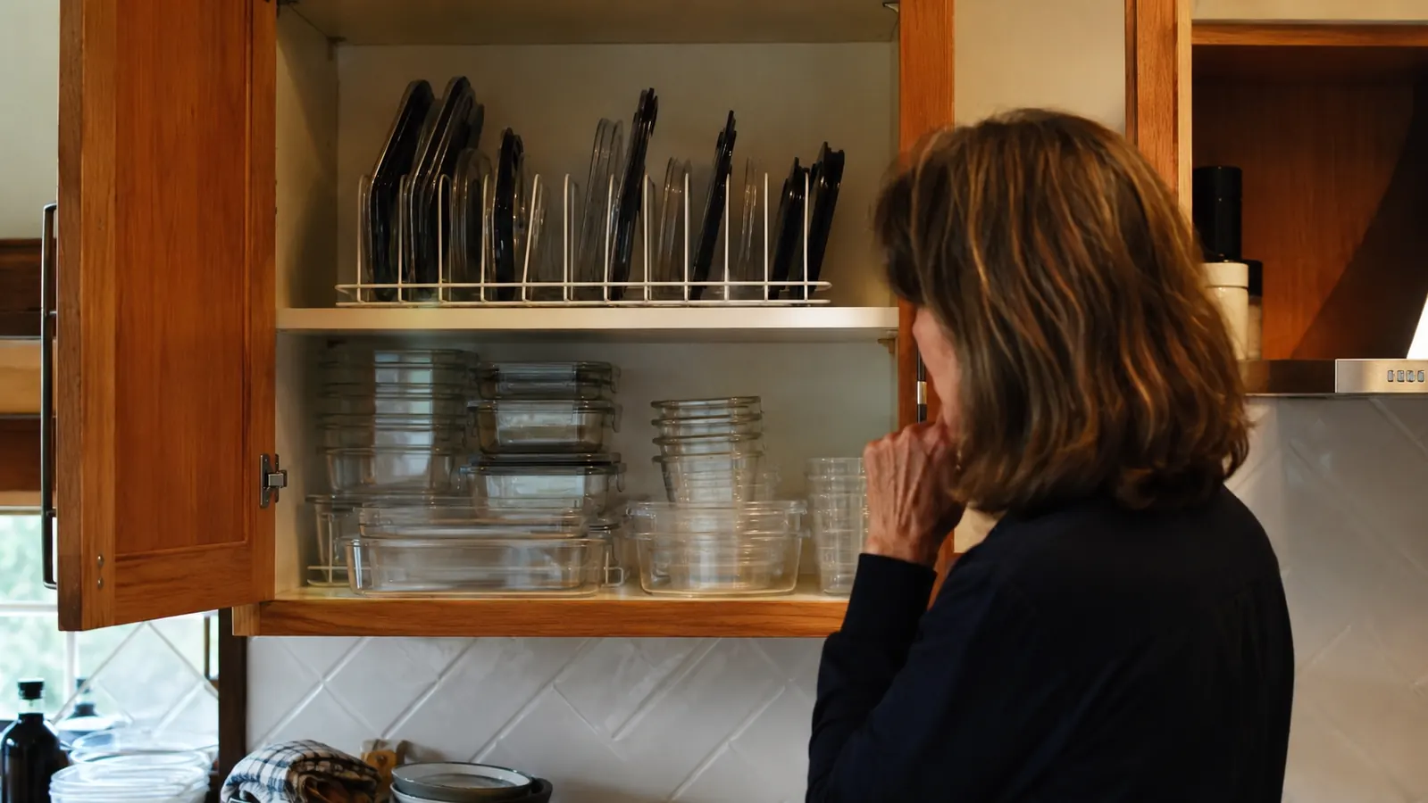 Stacked Rubbermaid Brilliance containers on one shelf with their lids stored separately upright in a dish rack on the shelf above